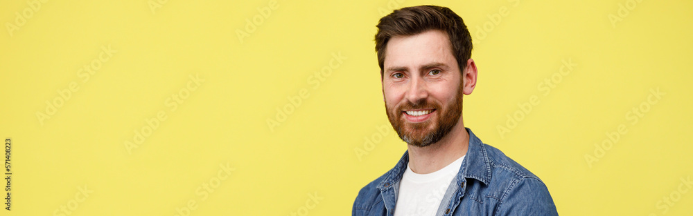 Fototapeta premium Handsome smiling man with beard holding laptop and looking at camera on yellow background