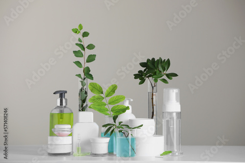 Many containers and glass tubes with leaves on white table against light grey background © New Africa