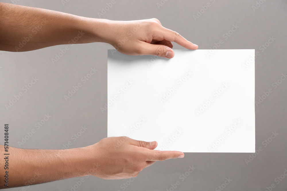 Man holding sheet of paper on grey background, closeup. Mockup for design Man holding sheet of paper on grey background, closeup. Mockup for design