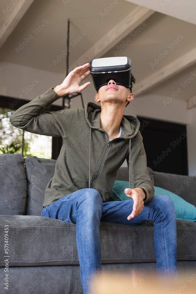 Vertical image of biracial teenage boy with vr headset sitting on sofa at home Vertical image of biracial teenage boy with vr headset sitting on sofa at home
