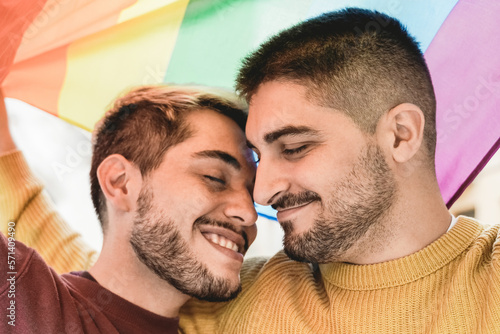 Happy gay men couple having tender moment under rainbow LGBT flag outdoor - Diversity love concept - Soft focus on right male face © Vane Nunes