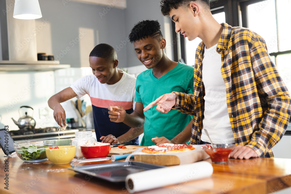 Happy diverse teenage male friends preparing pizza in kitchen Happy diverse teenage male friends preparing pizza in kitchen