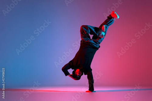young guy dancer break dancing in neon red blue lighting, active energetic man doing acrobatic tricks, crazy moves