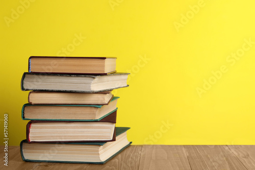 Stack of old hardcover books on wooden table against yellow background  space for text