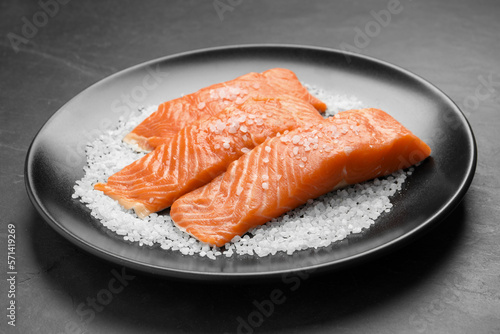 Fresh raw salmon with salt on black table, closeup