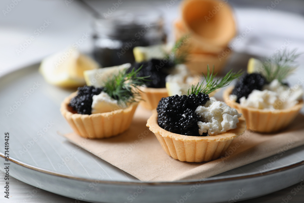 Delicious tartlets with black caviar, cream cheese and lemon served on light table, closeup Delicious tartlets with black caviar, cream cheese and lemon served on light table, closeup