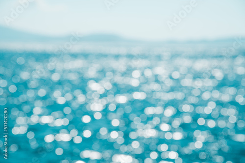 Blurred background of blue water and bokeh of sunlight hitting the sea with Mountain View and clear sky. Summer holiday backdrop.Mock up template for display or montage of product or content.