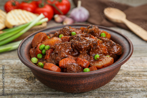 Delicious beef stew with carrots, peas and potatoes on wooden table, closeup