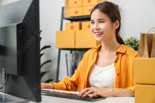 Canvas Print Startup small business, Young Asian woman checking online order on computer and packing boxes for products to send to customers