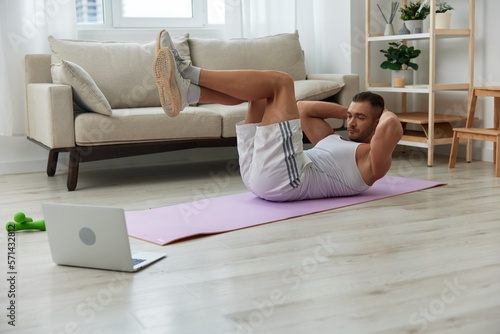 Man sports, watching tape of workout on phone and repeating exercises sports blogger with laptop training online, pumped up man fitness trainer works out at home, the concept of health and body beauty