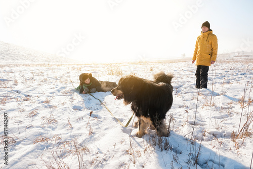 Father and son having fun with big black dog on winter background. Family winter activity with pet on sunny day outdoor