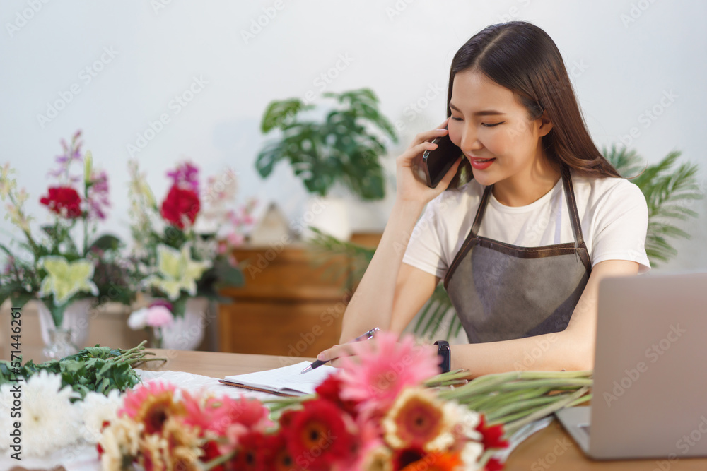 Flower shop concept, Female florist talking with customer on smartphone and taking note on notebook