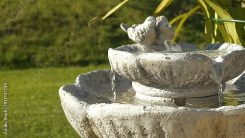 CLOSE UP: Decorative outdoor fountain with running water in green spring garden. Atmospheric garden water element with relaxing and calming effect. Cascading birdbath for hot and dry summer days. photo