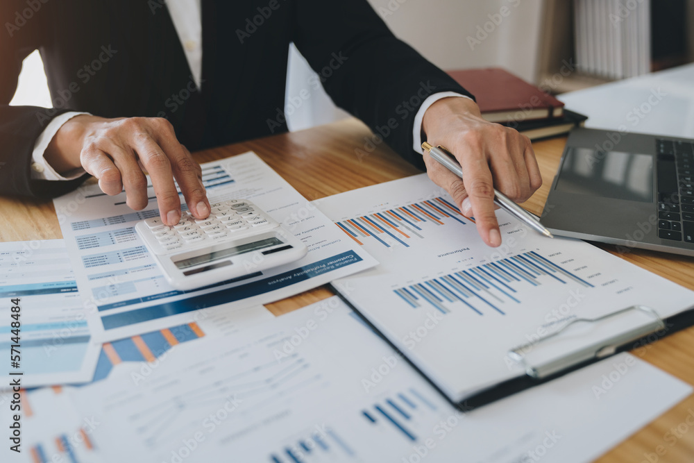 Asian businesswoman pressing calculator to calculate income tax and company income, finance, accounting, statistics graphs in real estate business in her office. Asian businesswoman pressing calculator to calculate income tax and company income, finance, accounting, statistics graphs in real estate business in her office.