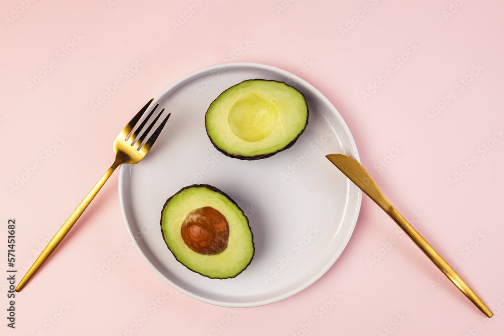 Avocado cut in halves on the plate and golden color flatware Avocado cut in halves on the plate and golden color flatware