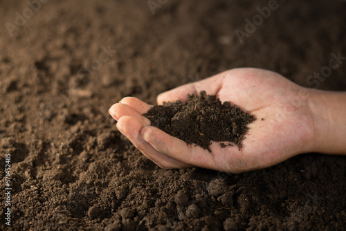 hand holding pile of soil with farmland background