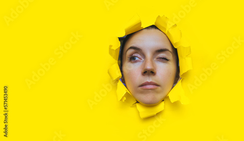 Fotografiet Close-up portrait of a caucasian young woman looking through a hole in yellow paper and winking