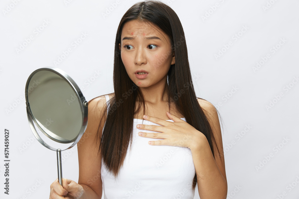 Asian woman with mirror in hand facial skin problems, acne and inflammation, red rash and allergies, chicken pox, sadness from rashes. Facial skin care concept for diseases and nerves Asian woman with mirror in hand facial skin problems, acne and inflammation, red rash and allergies, chicken pox, sadness from rashes. Facial skin care concept for diseases and nerves