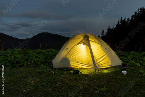 Luminous tourist tent in nature. Tourist tent and equipment. Camping. Tent at dusk. Glowing tent against the backdrop of mountains.