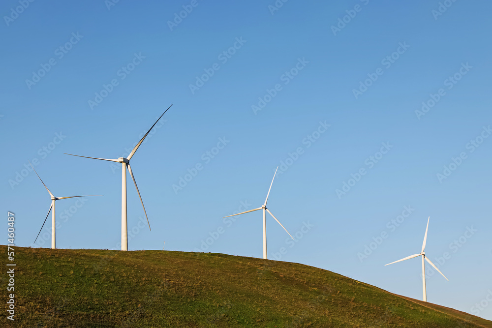 Wind power turbines on the green hill lover the blue sky.