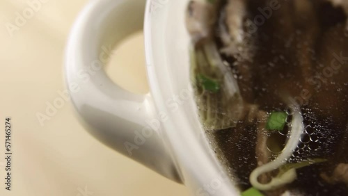 Boiled beef, green onions, red onions, broth. Fo Bo soup in a white bowl. Close-up.