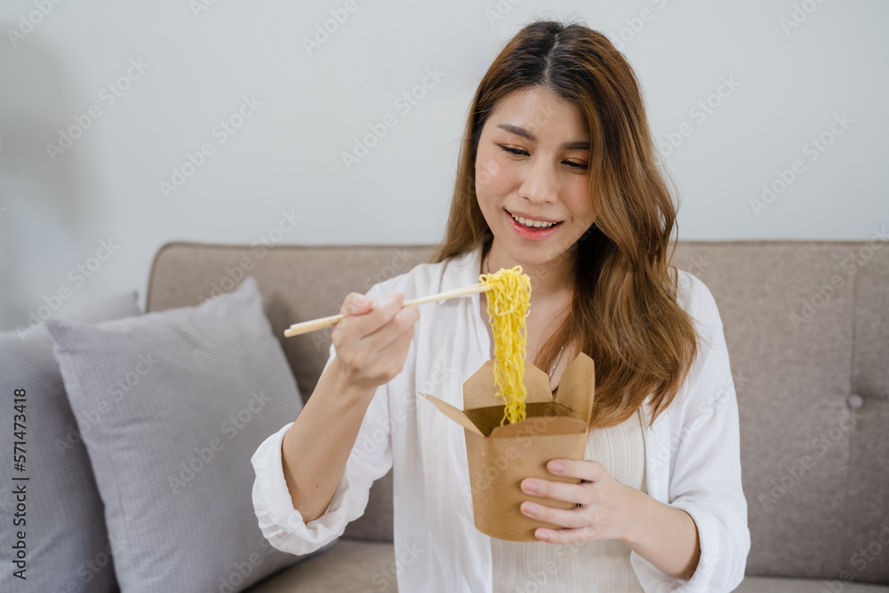 Food delivery. Happy asian woman eating noodles with chopsticks unpacking takeaway food at home. Food delivery. Happy asian woman eating noodles with chopsticks unpacking takeaway food at home.