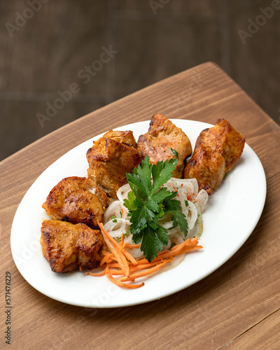 Pieces of fried meat garnished with fresh vegetables. Shashlik with carrots and onions garnished with parsley on white plate. Roasted chicken. Soft focus. Copy space. Top view.