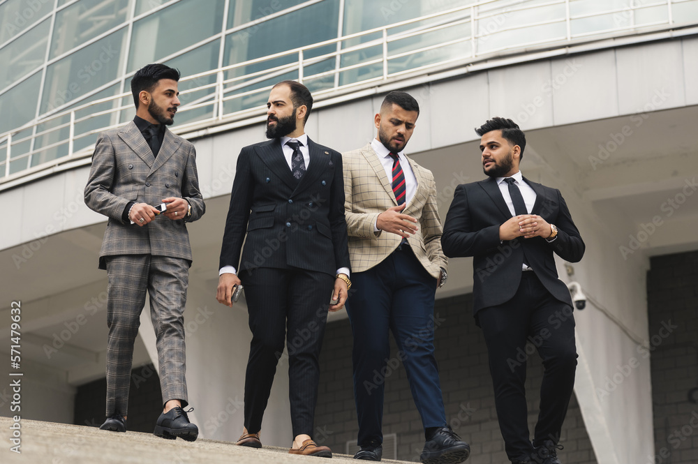 Business people outdoor meeting. A group of male businessmen in suits walk down the street stairs against the backdrop of a glass building. Working break. Teamwork and brainstorming. Business people outdoor meeting. A group of male businessmen in suits walk down the street stairs against the backdrop of a glass building. Working break. Teamwork and brainstorming.