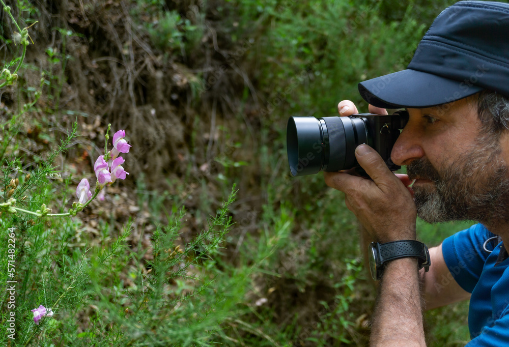 bearded man photographing a flower in the field