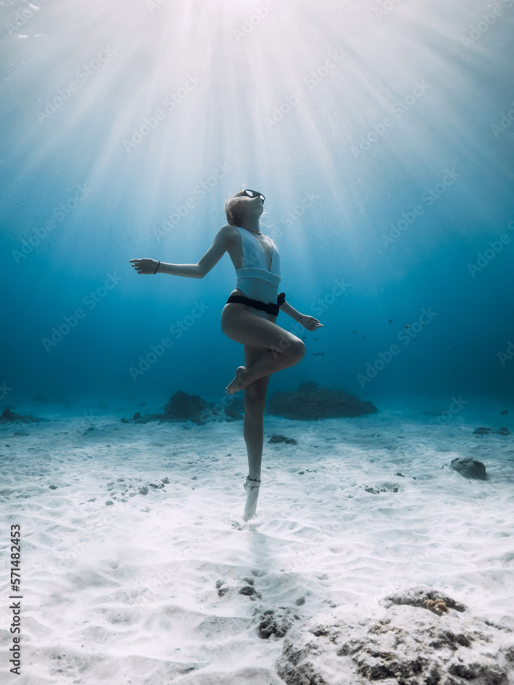 Freediver girl posing underwater. Free diving with woman in blue ocean with sandy bottom and sun rays