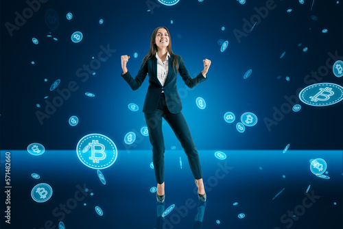 Happy young european business woman with falling digital bitcoins on blue background. Success, cryptocurrency exchange and money concept.