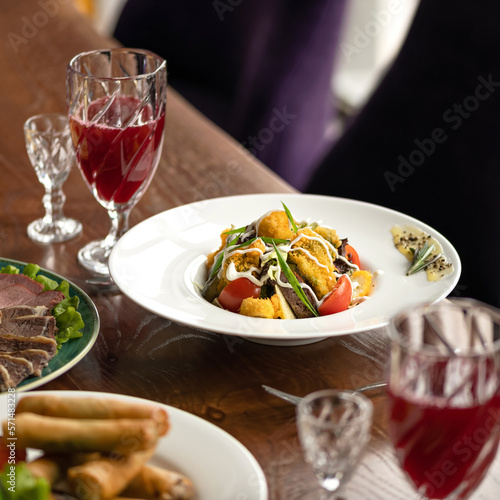 Lunch at restaurant for two people. Salad, cold appetizers, glasses with fruit drinks and glasses on table. Wooden table, purple armchair. Soft focus. Side view. 