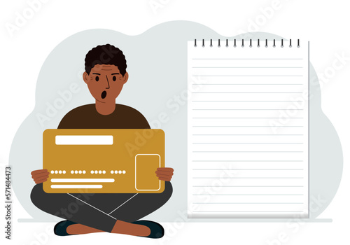 A man sits cross-legged in his hands holding a large credit card next to a close-up notepad for text. Concept of credit card, expense planning, income planning.