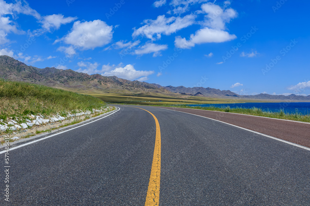 Empty asphalt road and lake with mountain natural scenery in Xinjiang, China.