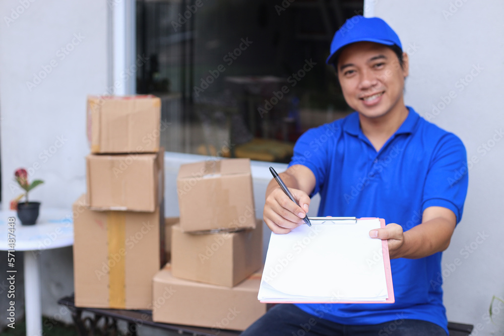 Young deliveryman showing shipping document to be signed while sitting with pile of boxes to send to customers outside the office. Young deliveryman showing shipping document to be signed while sitting with pile of boxes to send to customers outside the office.