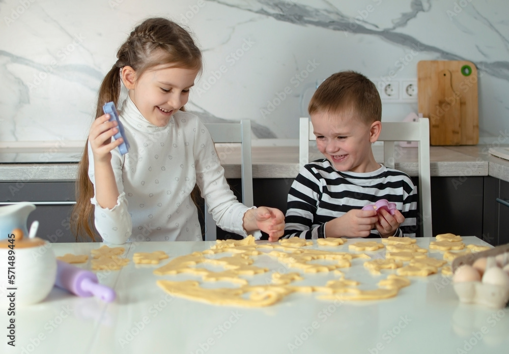 Cheerful children bake cookies in white kitchen. Little girl likes to cook in kitchen. Happy child cooks dough, bakes cookies in kitchen. Children learn new things. Concept of children's leisure