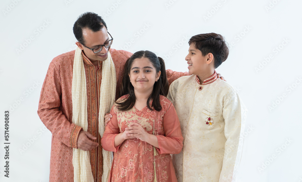 Portrait of happy Indian family handsome teenage son, little daughter and father embracing standing and talking, wearing traditional clothing. Family love bonding concept. White background Portrait of happy Indian family handsome teenage son, little daughter and father embracing standing and talking, wearing traditional clothing. Family love bonding concept. White background