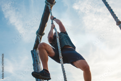 Below-view of a strong male pulling himself up a rope against blue sky photo