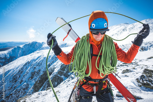 Ski mountaineer coiling rope with snowy mountains behind photo