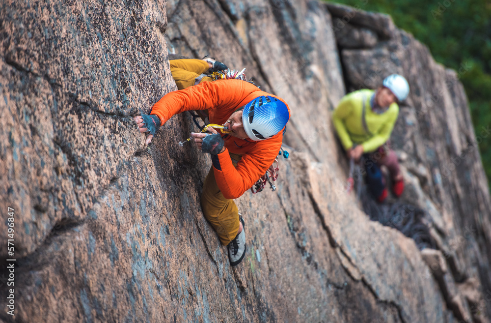 Man rock climbing on rock face with belayer below