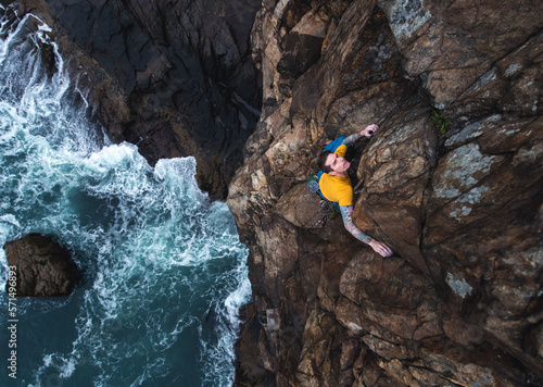 Man rock climbing on seaside cliff with waves crashing below photo