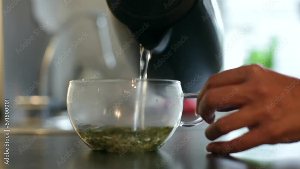 Lockdown shot of woman pouring hot water in transparent cup with tea leaves on kitchen counter at home Lockdown shot of woman pouring hot water in transparent cup with tea leaves on kitchen counter at home