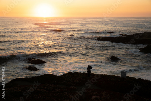 Backlit young woman photographing sunset over the ocean