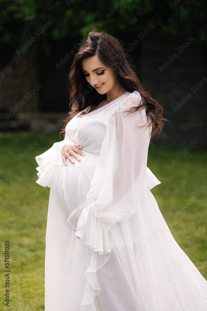 Elegant pregnant woman in beautiful white dress walking outdoors Elegant pregnant woman in beautiful white dress walking outdoors