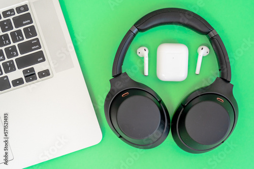 Laptop with big and small wireless headphones on green background