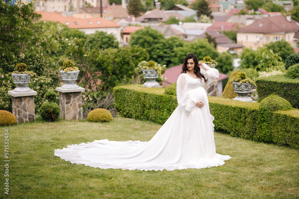 Elegant pregnant woman in beautiful white dress walking outdoors