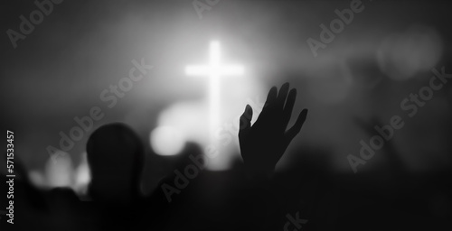 Passionate Christian praising with hands raised towards the cross and Holy Spirit filled gracious church worship with bokeh and silhouette background
