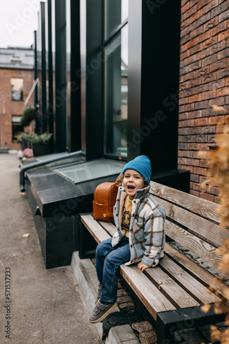 Little happy boy, outdoors, sitting on a wooden bench, laughing.