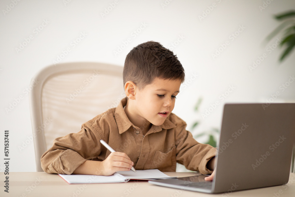 Busy cheerful european small kid has video call with teacher, tutor at computer at table in elementary school Busy cheerful european small kid has video call with teacher, tutor at computer at table in elementary school