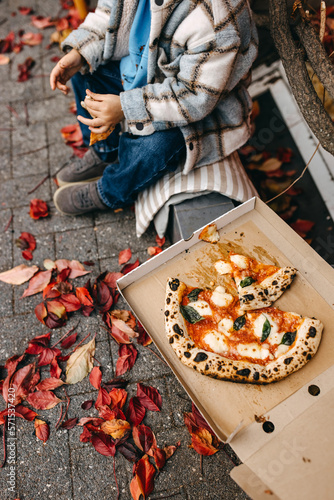 Fototapeta Naklejka Na Ścianę i Meble -  Take away pizza in a box outdoors. Child eating traditional margherita pizza.
